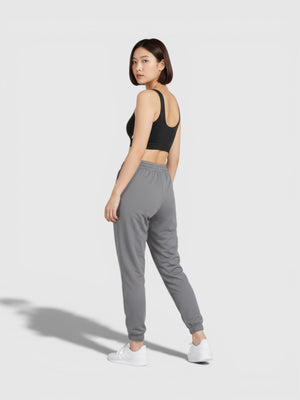 Model wanita mengenakan Adidas Purel LS Bra hitam dengan celana jogger abu-abu dan sepatu putih, tampak belakang.