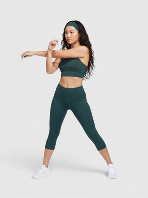 Model wanita mengenakan set olahraga Adidas Powerimpact hijau tua dengan bra medium-support dan legging 3/4
