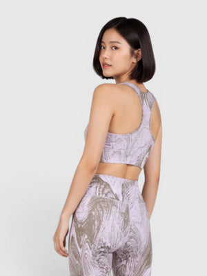 Model wanita mengenakan set olahraga Adidas by Stella McCartney TruePurpose dengan motif marmer ungu dan abu-abu