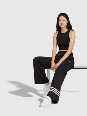 Model wanita mengenakan celana trackpants hitam Adidas Adicolor Neuclassics dengan detail 3-Stripes putih di kaki