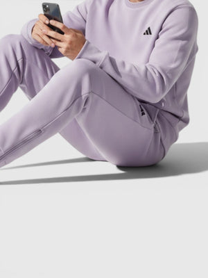 Pria mengenakan setelan celana jogger Adidas W Z.N.E. warna ungu muda dengan detail ritsleting dan bahan lembut.