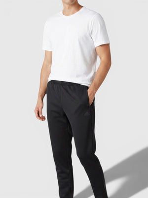 Pria mengenakan celana jogger hitam Adidas dari FTFO || BIG BRAND LOW PRICE dengan kaos putih dan sepatu sneakers.