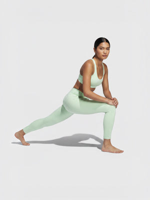 Model wanita mengenakan set legging dan bra olahraga Adidas All Me MM 7/8 warna hijau mint untuk yoga dan pilates