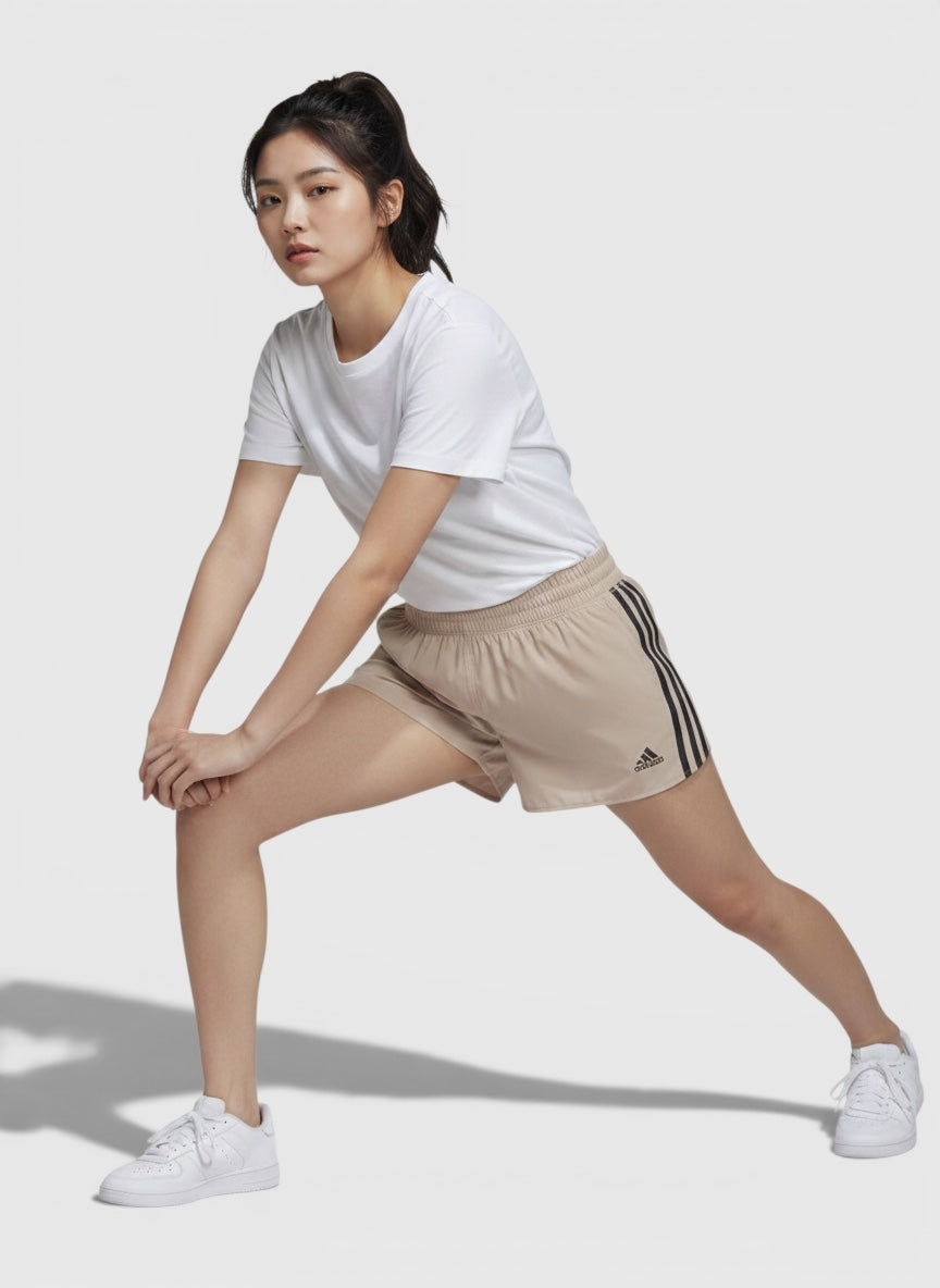 Wanita mengenakan celana lari Adidas Run Icons 3-Stripes berwarna krem dengan detail garis reflektif dari FTFO