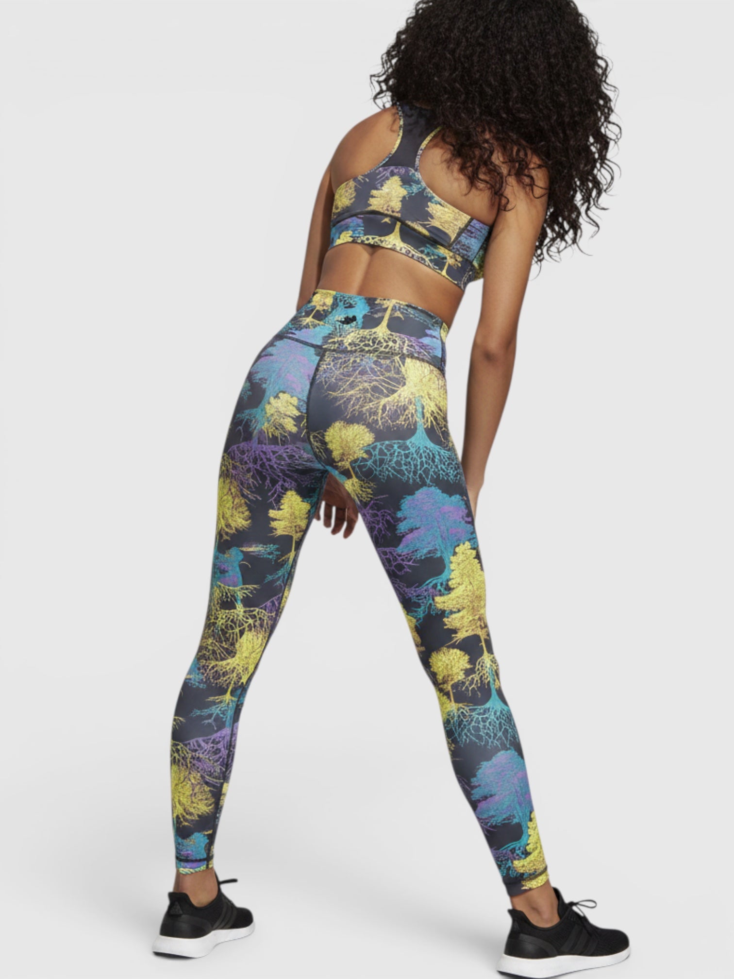 Model mengenakan set olahraga Adidas by Stella McCartney dengan motif pohon warna-warni dan desain racer-back dari FTFO