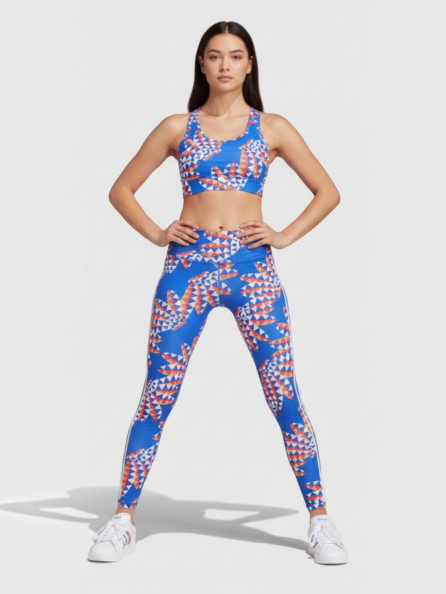 Model mengenakan set legging dan sport bra Adidas x FARM Rio berwarna biru dengan motif geometris tropis yang ceria.