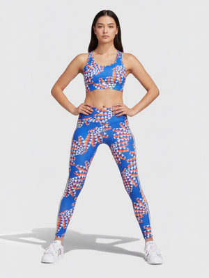 Model mengenakan set legging dan sport bra Adidas x FARM Rio berwarna biru dengan motif geometris tropis yang ceria.