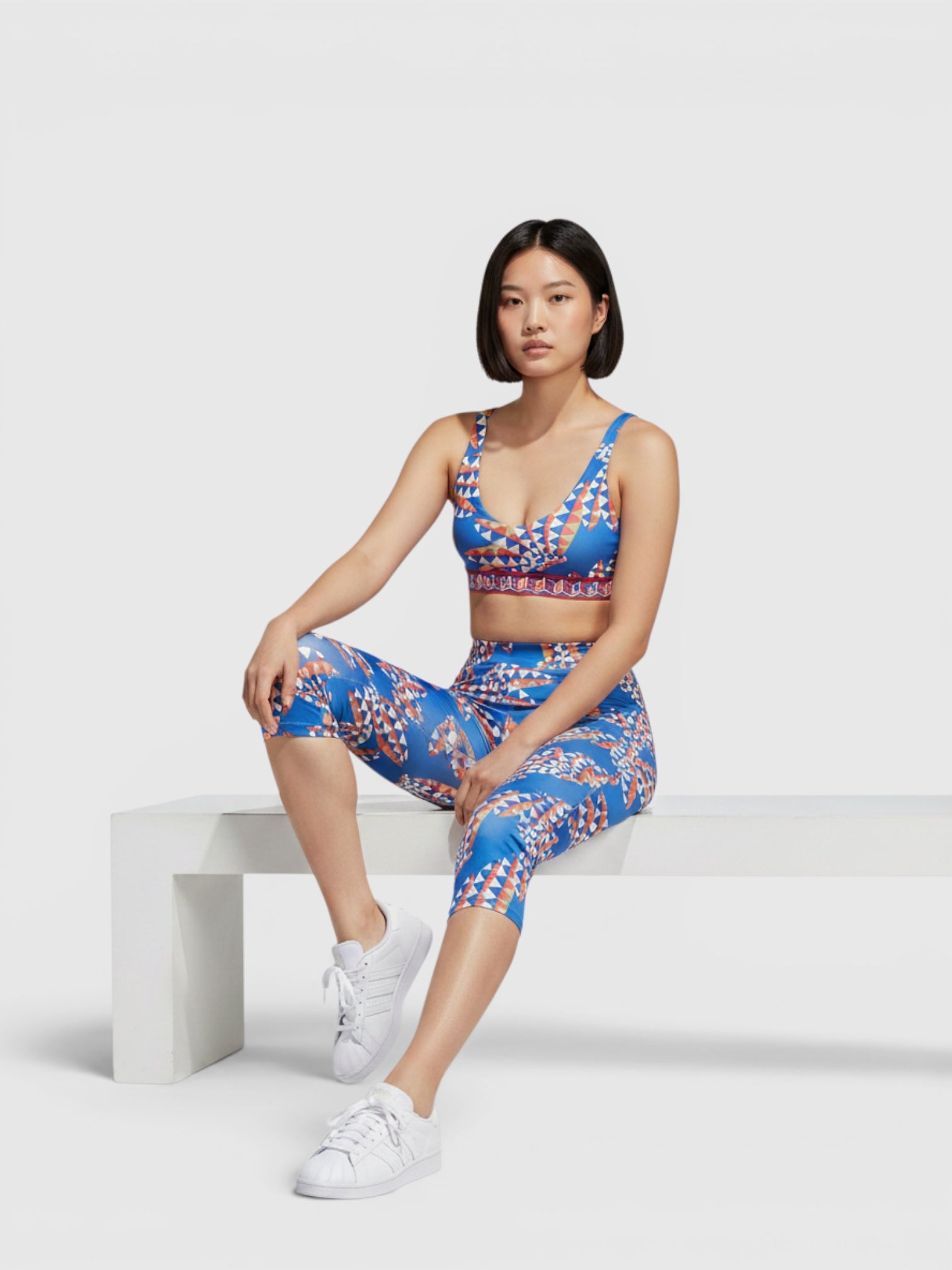 Model mengenakan set olahraga Adidas x FARM Rio berwarna biru dengan motif kaleidoskopik oranye, bra medium-support dan legging.
