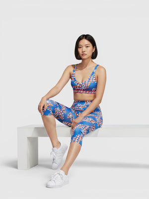 Model mengenakan set olahraga Adidas x FARM Rio berwarna biru dengan motif kaleidoskopik oranye, bra medium-support dan legging.