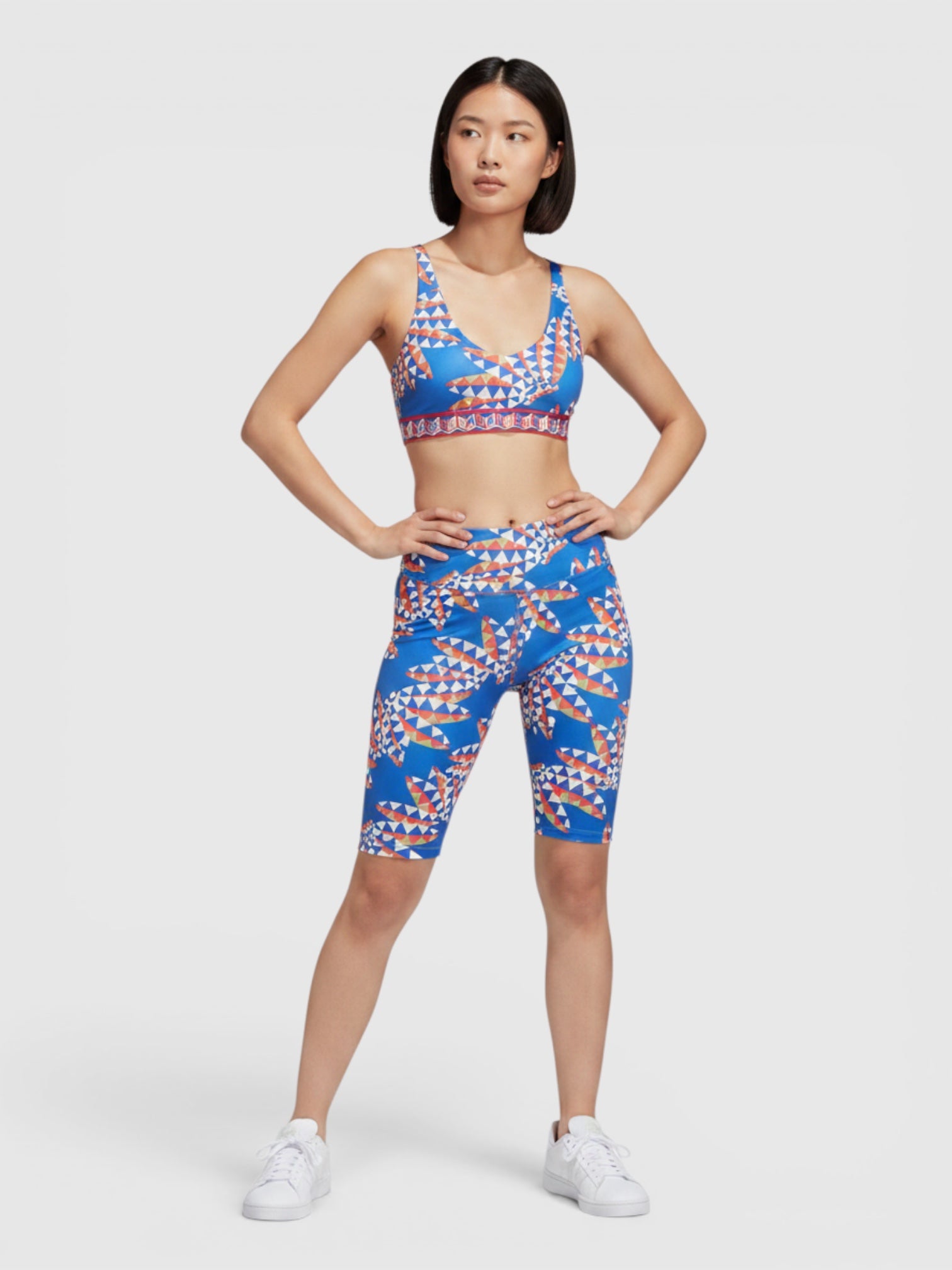 Model mengenakan set olahraga Adidas x FARM Rio biru bermotif kaleidoskopik dengan bra medium-support dan celana pendek