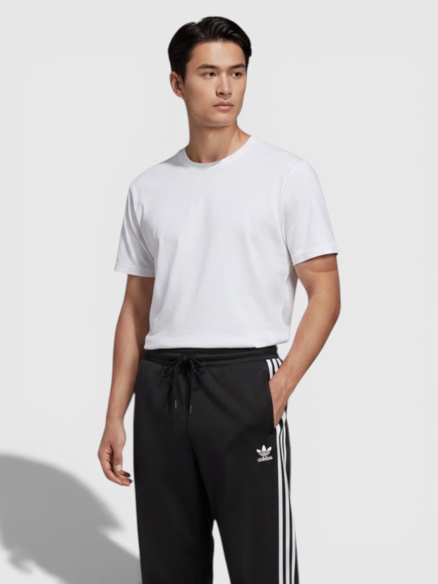Pria mengenakan celana jogger Adidas hitam dengan tiga garis putih ikonik dan tali pinggang dari FTFO || BIG BRAND LOW PRICE