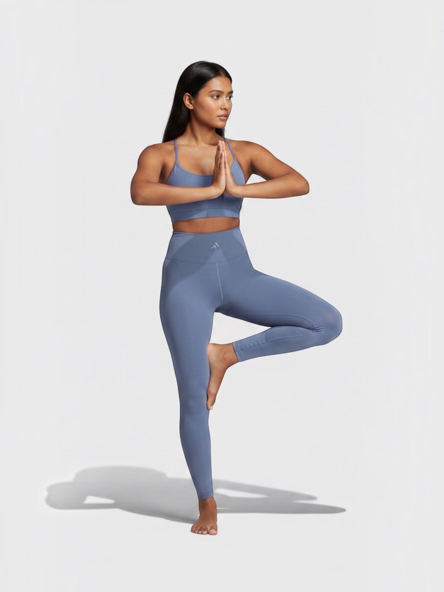 Model wanita mengenakan set legging dan bra olahraga Adidas All Me 7/8 berwarna biru saat melakukan pose yoga