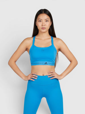 Model mengenakan Adidas by Stella McCartney TruePurpose medium support sport bra biru cerah dengan desain racerback.