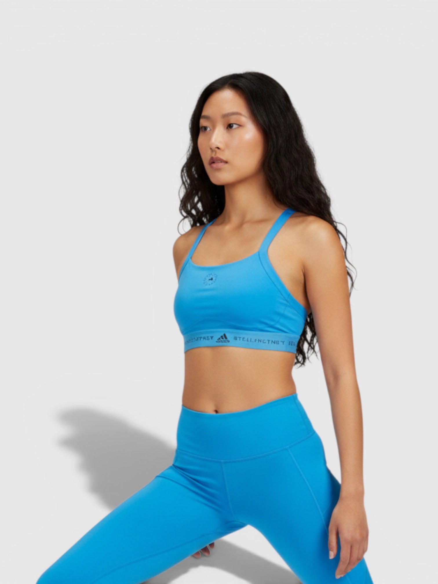 Model mengenakan Adidas by Stella McCartney TruePurpose medium support sport bra berwarna biru cerah dengan detail logo