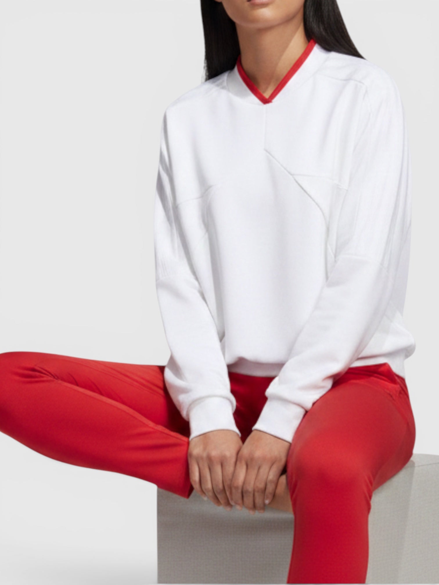 Model wanita mengenakan sweatshirt putih Adidas W Tiro Crew dengan aksen kerah merah dan celana legging merah senada.