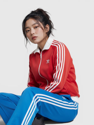 Model wanita mengenakan jaket track merah Adidas dan celana track biru dengan detail 3-Stripes ikonik dari FTFO || BIG BRAND LOW PRICE