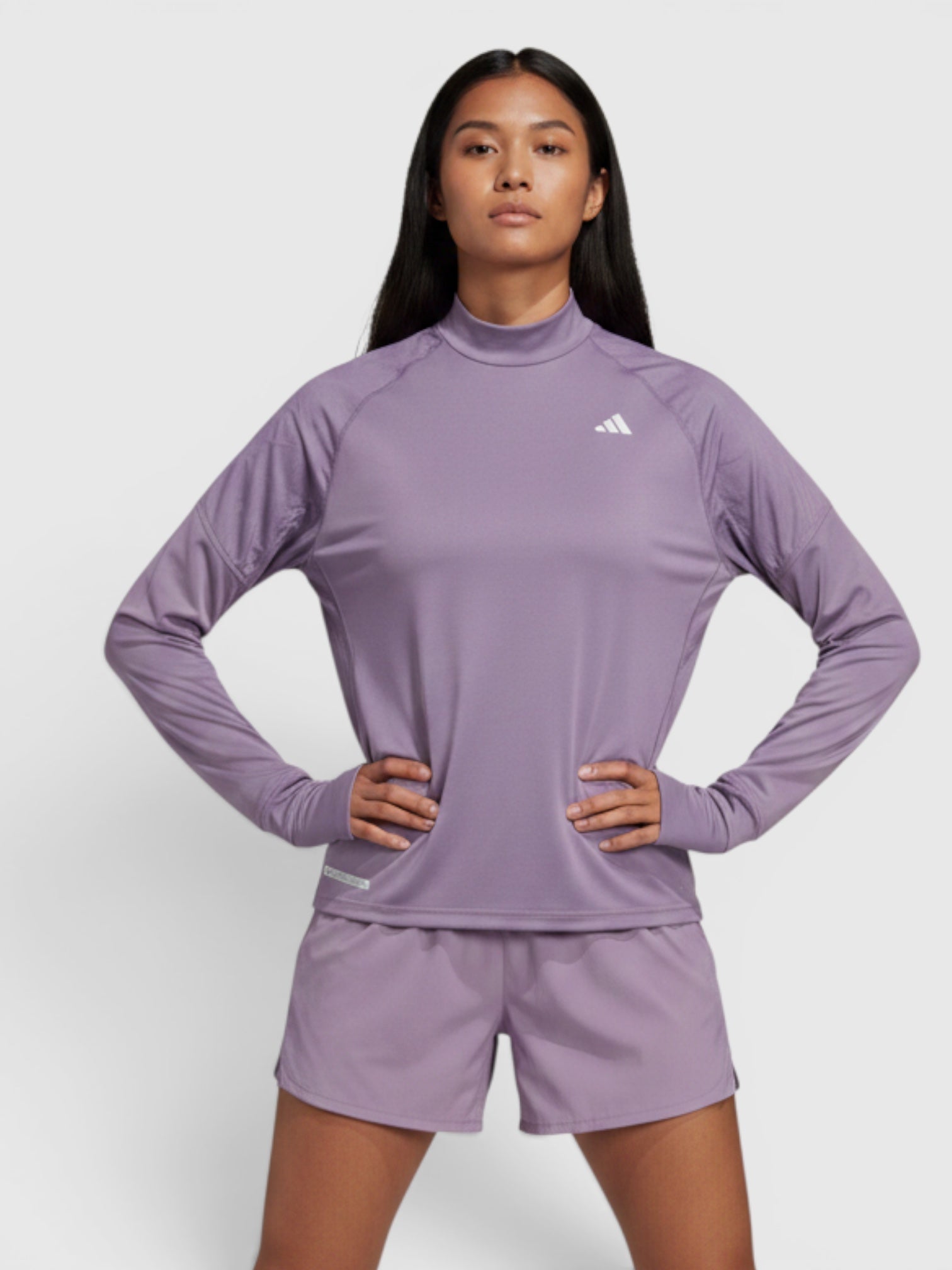 Model wanita mengenakan Adidas Ultimate Sweatshirt berwarna ungu dengan kerah tinggi, lubang ibu jari, dan teknologi AEROREADY dari FTFO || BIG BRAND LOW PRICE