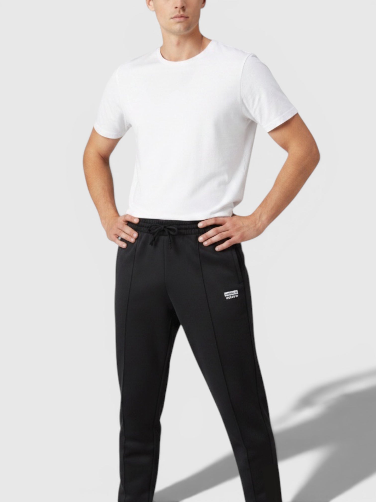 Model pria mengenakan celana jogger hitam Adidas dari FTFO || BIG BRAND LOW PRICE dengan kaos putih dan sepatu kets