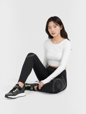 Model wanita mengenakan celana lari ketat Adidas berwarna hitam dengan detail reflektif dan atasan putih di studio