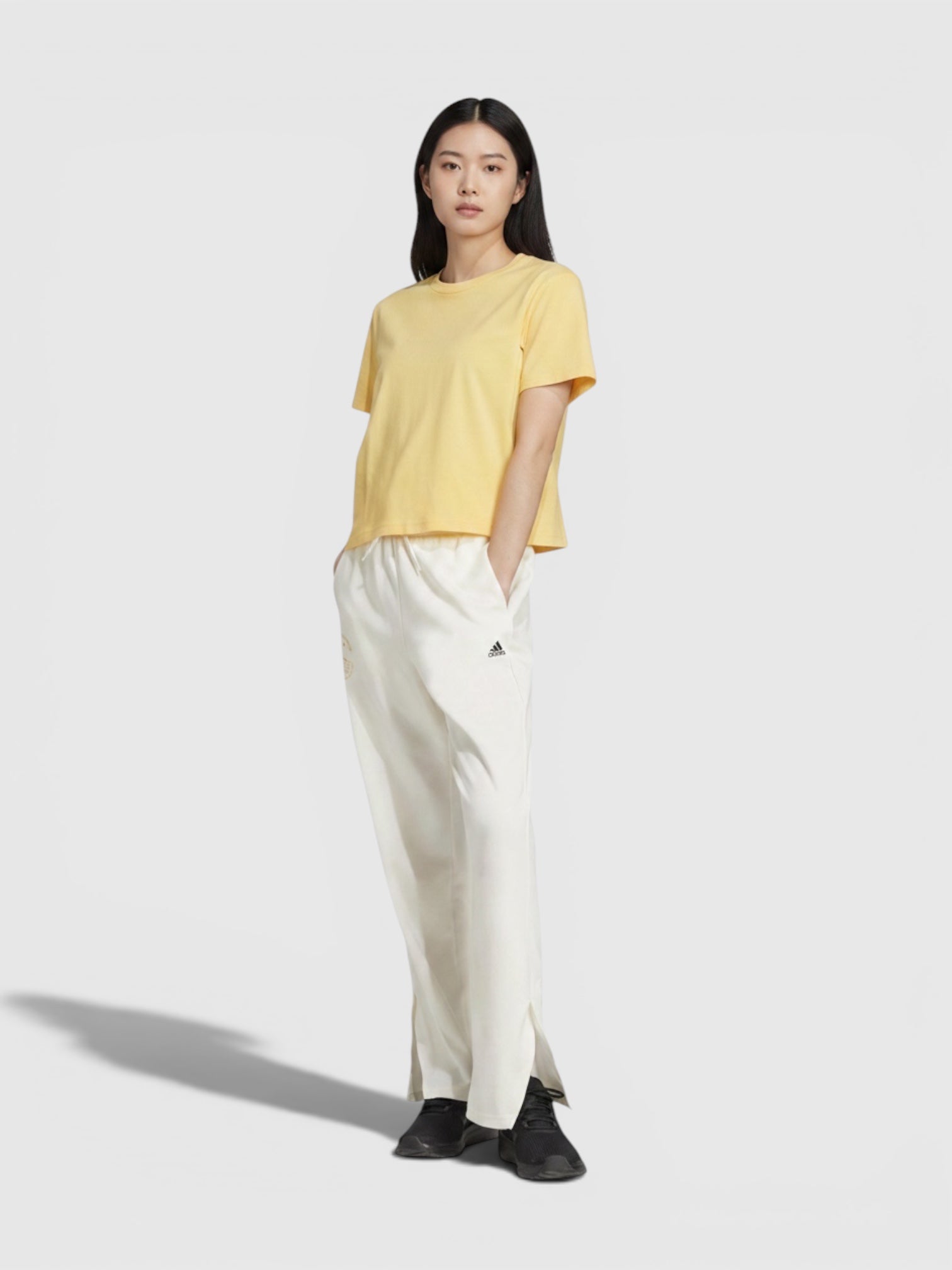 Model wanita mengenakan celana olahraga putih Adidas W Response Pants dengan pinggang elastis dan kaos kuning