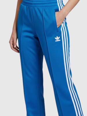 Celana track Adidas Adicolor Classics biru dengan 3-Stripes putih, logo Trefoil, dan saku ritsleting dari FTFO