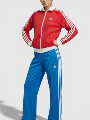 Model wanita mengenakan celana track Adidas Adicolor Classics Oversized SST biru dengan detail 3-Stripes putih dari FTFO || BIG BRAND LOW PRICE