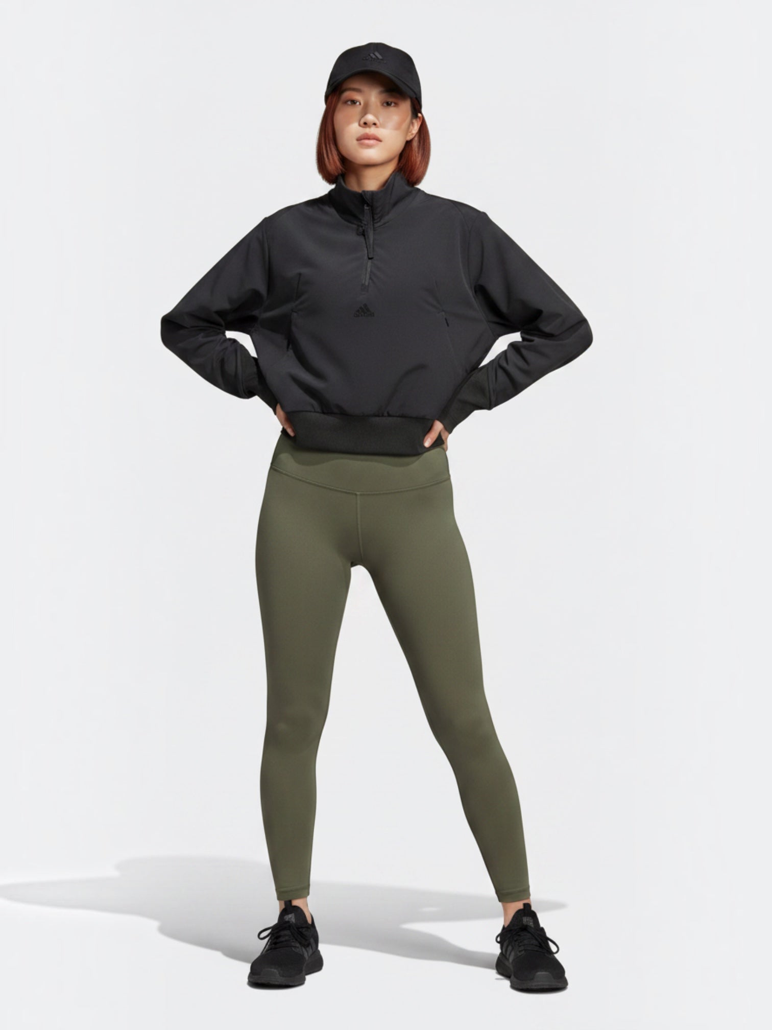 Model wanita mengenakan jaket Adidas Z.N.E. WVN QZ hitam dengan quarter-zip, celana legging hijau zaitun, dan topi dari FTFO || BIG BRAND LOW PRICE