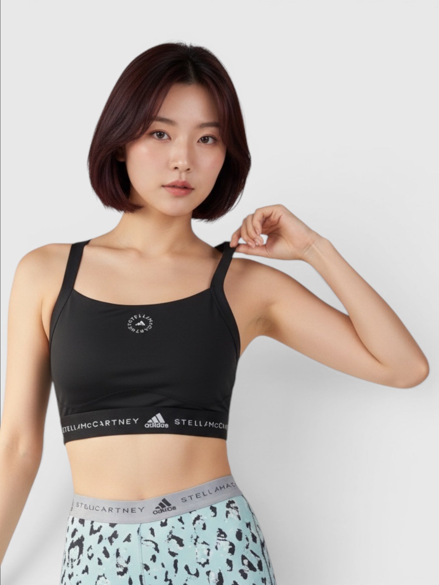 Model mengenakan sport bra hitam Adidas by Stella McCartney TruePurpose dengan logo ikonik dan desain racerback modern.