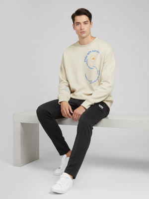 Pria mengenakan sweatshirt oversize krem FTFO || BIG BRAND LOW PRICE dengan grafis melingkar dan logo di dada.