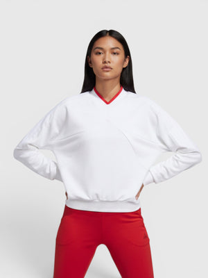 Model wanita mengenakan sweatshirt putih Adidas W Tiro Crew dengan aksen kerah merah dan celana panjang merah senada.